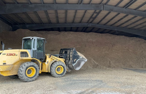 A payloader sits in the entrance of a storage building filled to the ceiling with wood chips